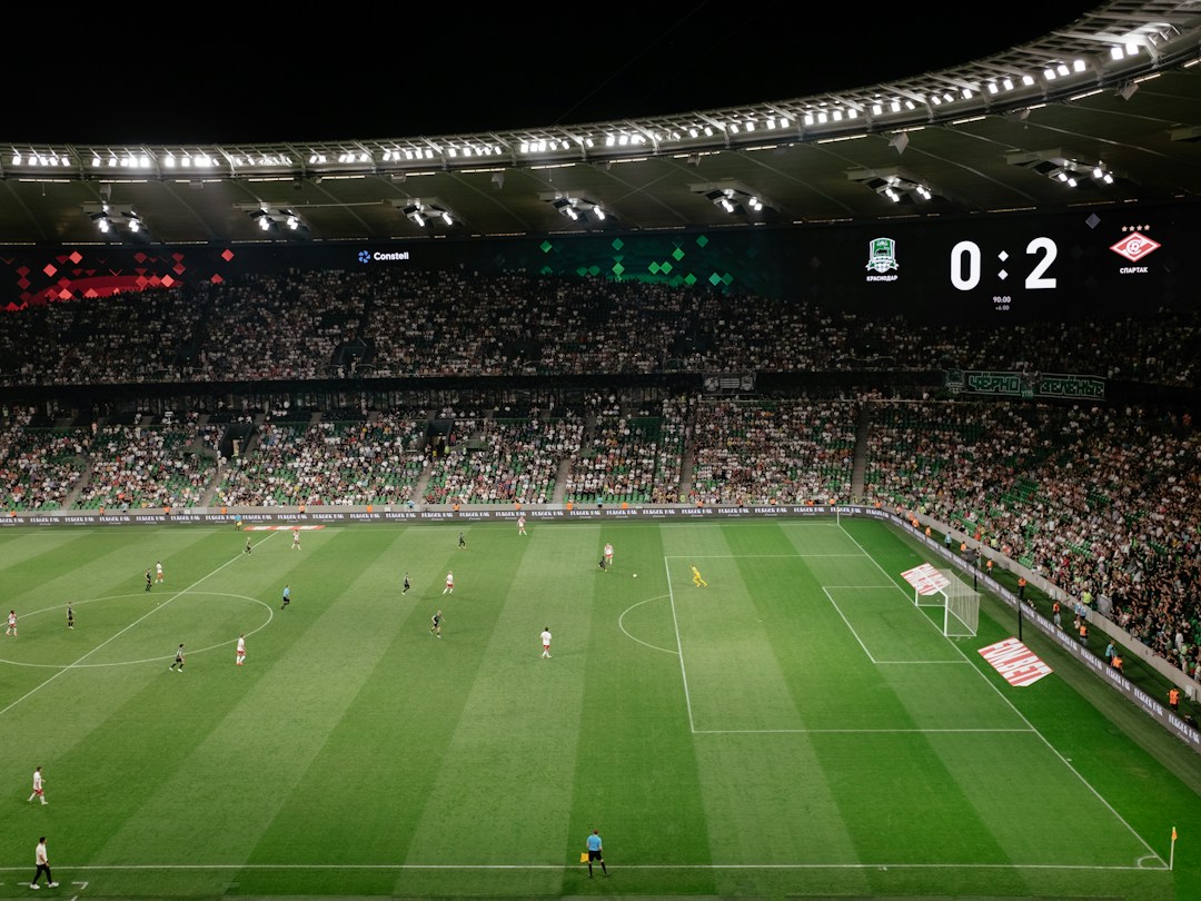 Premier League football stadium and pitch illuminated by floodlights ahead of an evening match, Unsplash photograph by Dmitry Ant